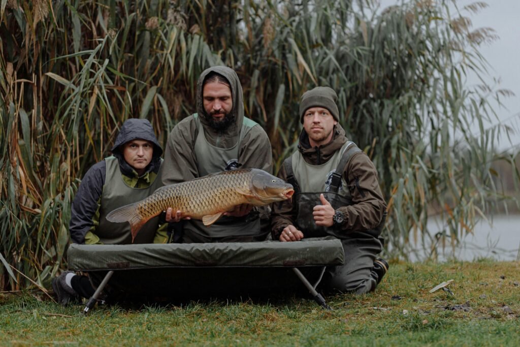 pexels-photo-5538150-5538150 Three fishermen proudly displaying a freshly caught carp beside a riverbank.