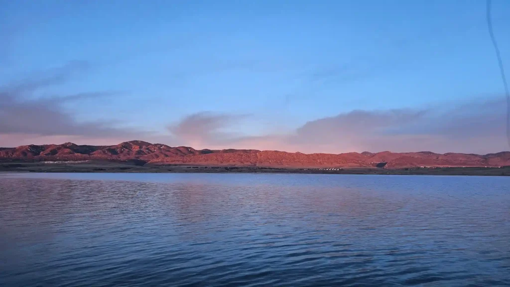 Calm summer lake at sunrise with mountains reflecting on the water, a prime location for bluegill fishing during summer.